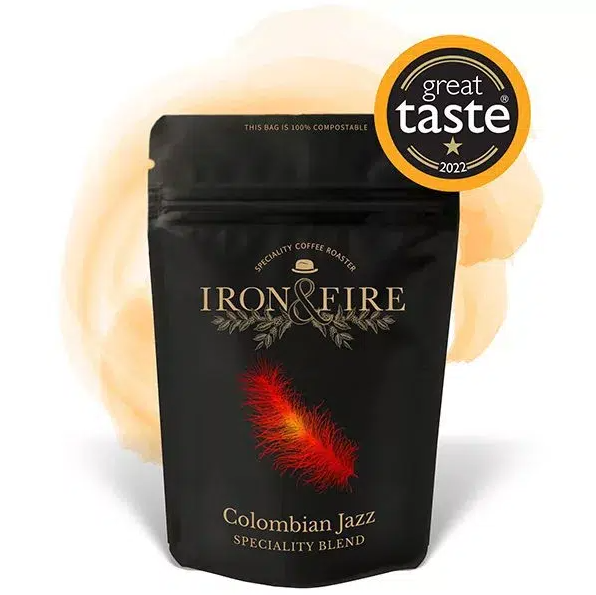 Iron & Fire Colombian Jazz Coffee Beans, sourced from the Huila region and winner of a 2022 Great Taste award, come in black packaging with a colorful red, orange, and yellow feather design. It is 100% compostable and Rainforest Alliance certified.