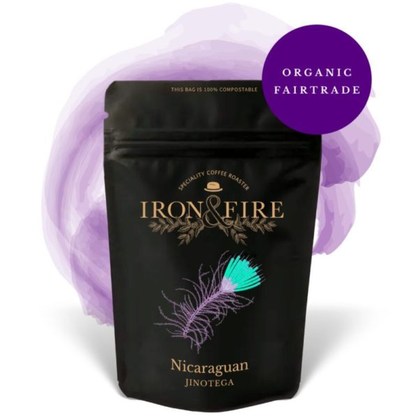 Adorned in black with a purple and turquoise feather design, the Iron & Fire Nicaraguan Jinotega Organic Aldea Coffee Beans bag features a purple circle confirming its Organic Fairtrade. A watercolor splash hints at a honey finish, perfect for espresso-based drinks.