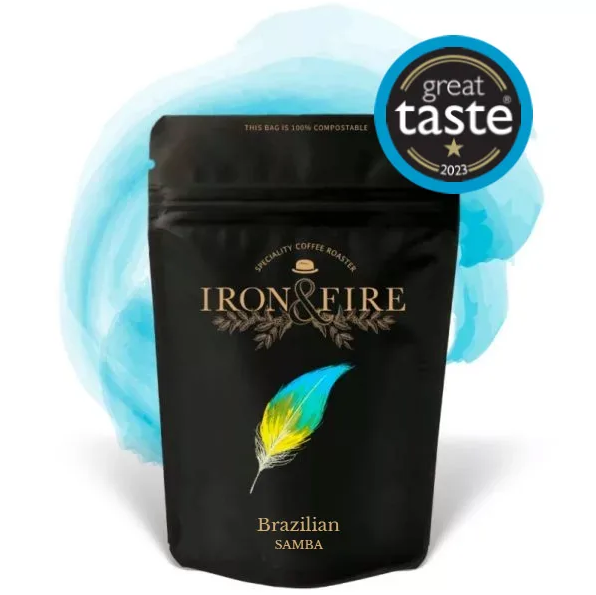 A black Iron & Fire Brazilian Samba coffee bag features a colorful feather design, with Great Taste 2023 award badge on the top right against a light blue watercolor backdrop. Known for its nutty flavor, this versatile coffee is ideal for great espresso.